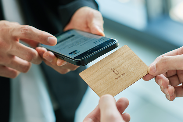 ナチュラルウッドのカードを手渡しながらスマートフォンにプロフィールを表示する利用シーン